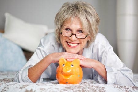 An old lady smiling at the camera leaning on a piggy bank
